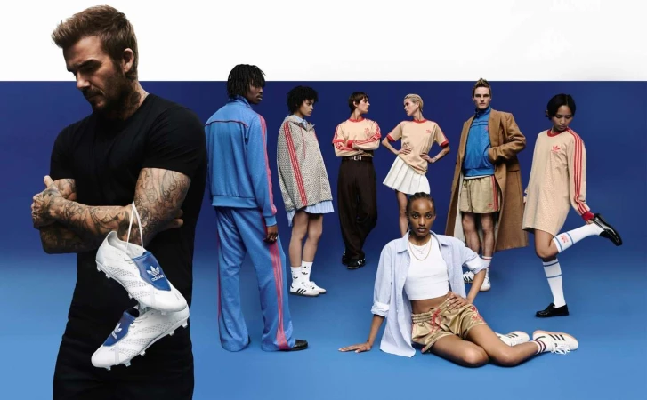 David Beckham holds Adidas soccer shoes among a group of diverse models showcasing Adidas athletic apparel on a blue and white backdrop.