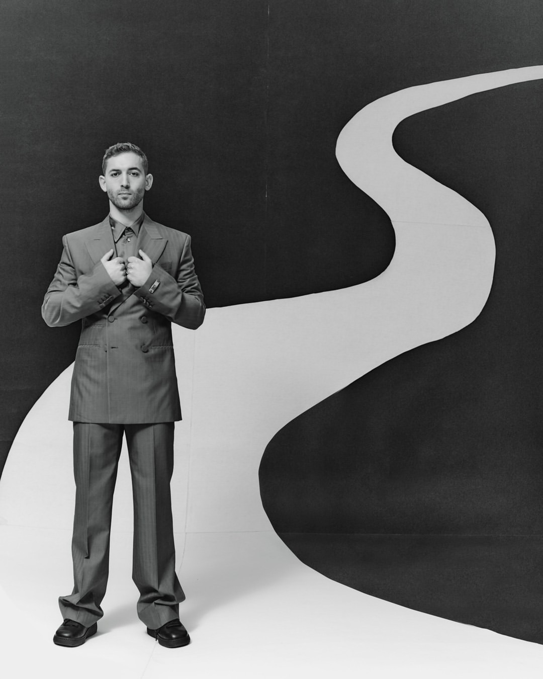 Monochrome portrait of a man in a suit posing against a black and white backdrop with a winding path design in a studio setting.