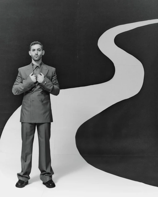 Monochrome portrait of a man in a suit posing against a black and white backdrop with a winding path design in a studio setting.