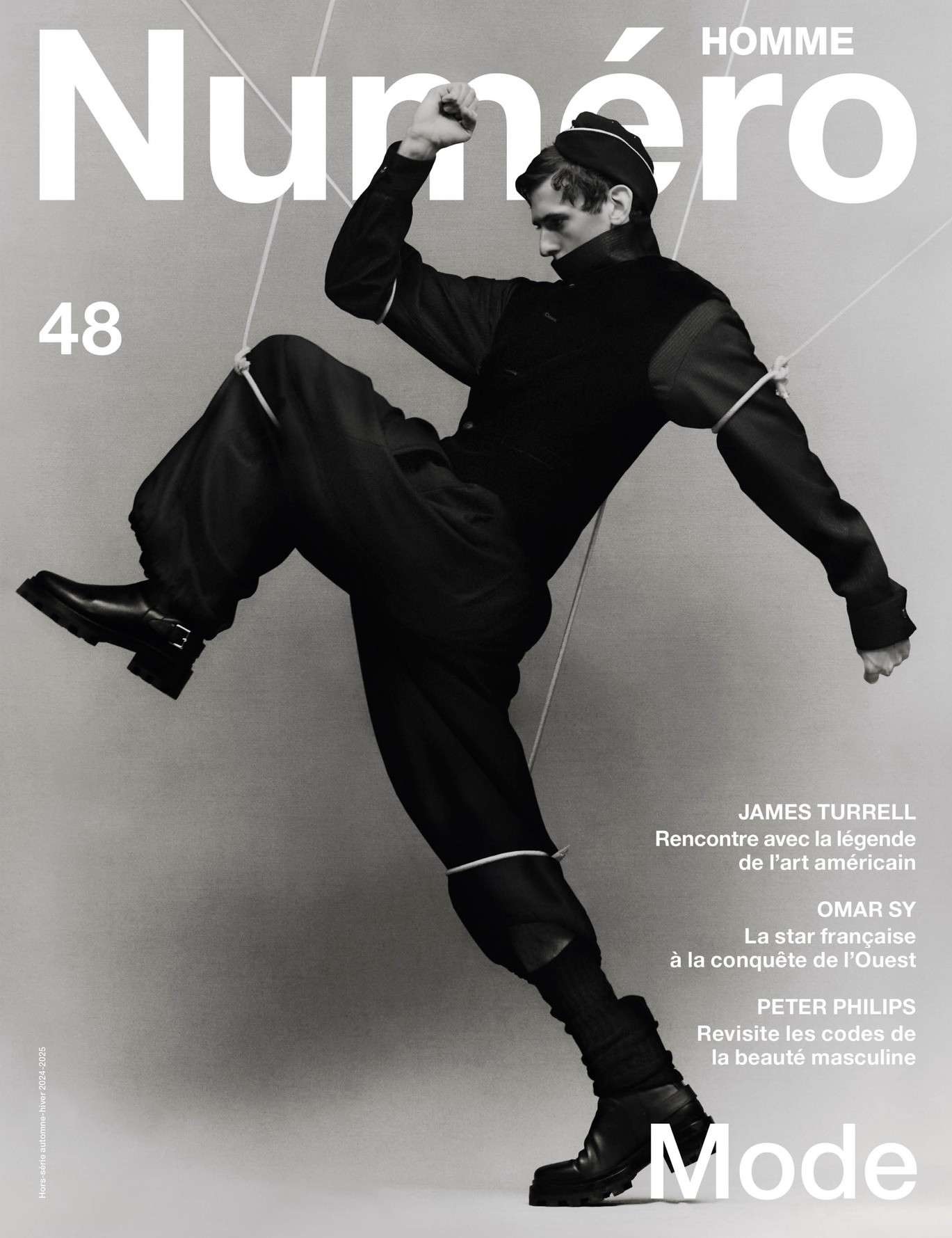 Fashion magazine cover featuring a male model in black attire and boots, dynamically posed against a gradient grey backdrop.
