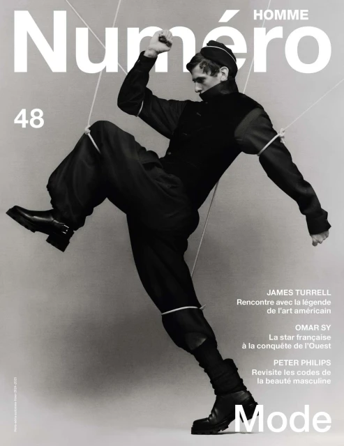 Fashion magazine cover featuring a male model in black attire and boots, dynamically posed against a gradient grey backdrop.