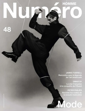 Fashion magazine cover featuring a male model in black attire and boots, dynamically posed against a gradient grey backdrop.