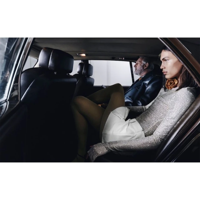 Fashion editorial featuring two people in a vintage car, one wearing a silver dress and the other in a leather jacket.
