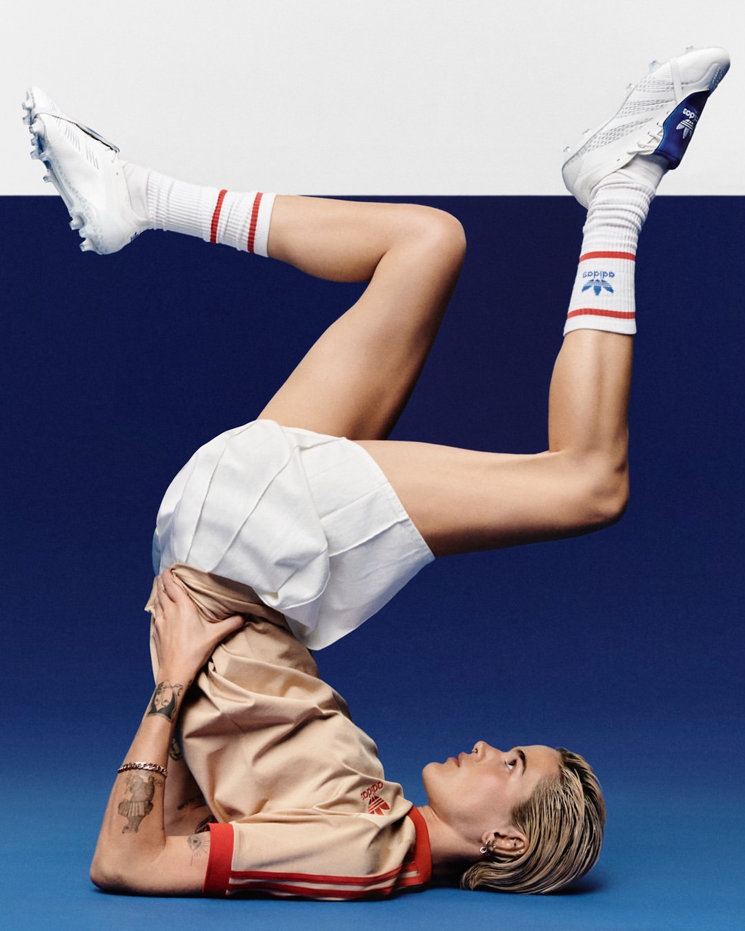 Athletic woman in sportswear does a yoga pose wearing Adidas clothing against a split blue and white background in a studio setting.