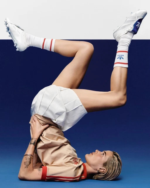Athletic woman in sportswear does a yoga pose wearing Adidas clothing against a split blue and white background in a studio setting.