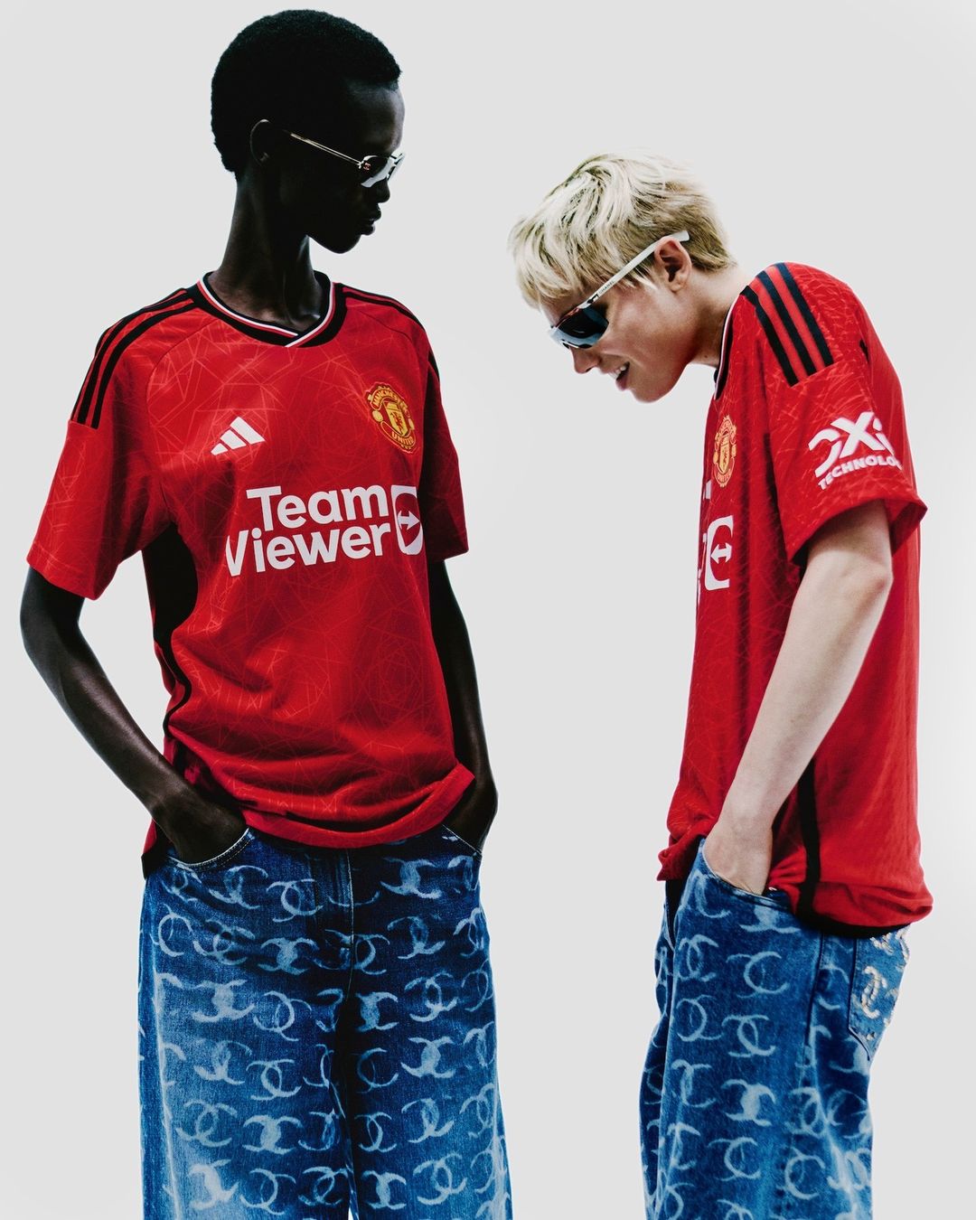 Two people pose wearing soccer jerseys and patterned jeans in a studio shot with bright lighting and a neutral background.