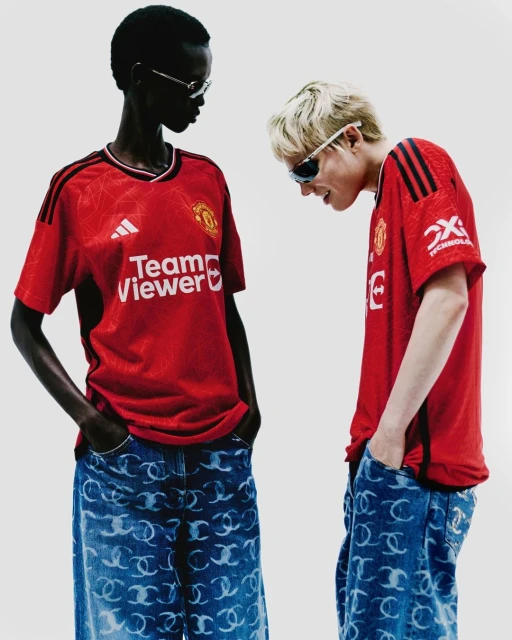 Two people pose wearing soccer jerseys and patterned jeans in a studio shot with bright lighting and a neutral background.