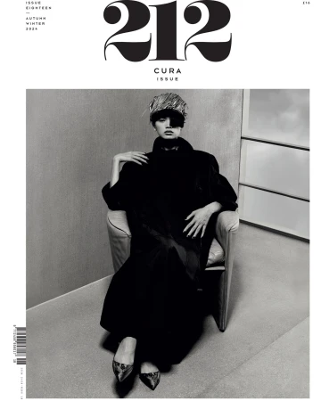Black and white magazine cover featuring a woman in a chair, wearing a distinctive hat and coat, with the magazine's title at the top.
