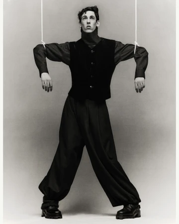 Monochrome image of a fair-skinned male in a dark vest and pants, mimicking a puppet, with strings attached to his arms and head.