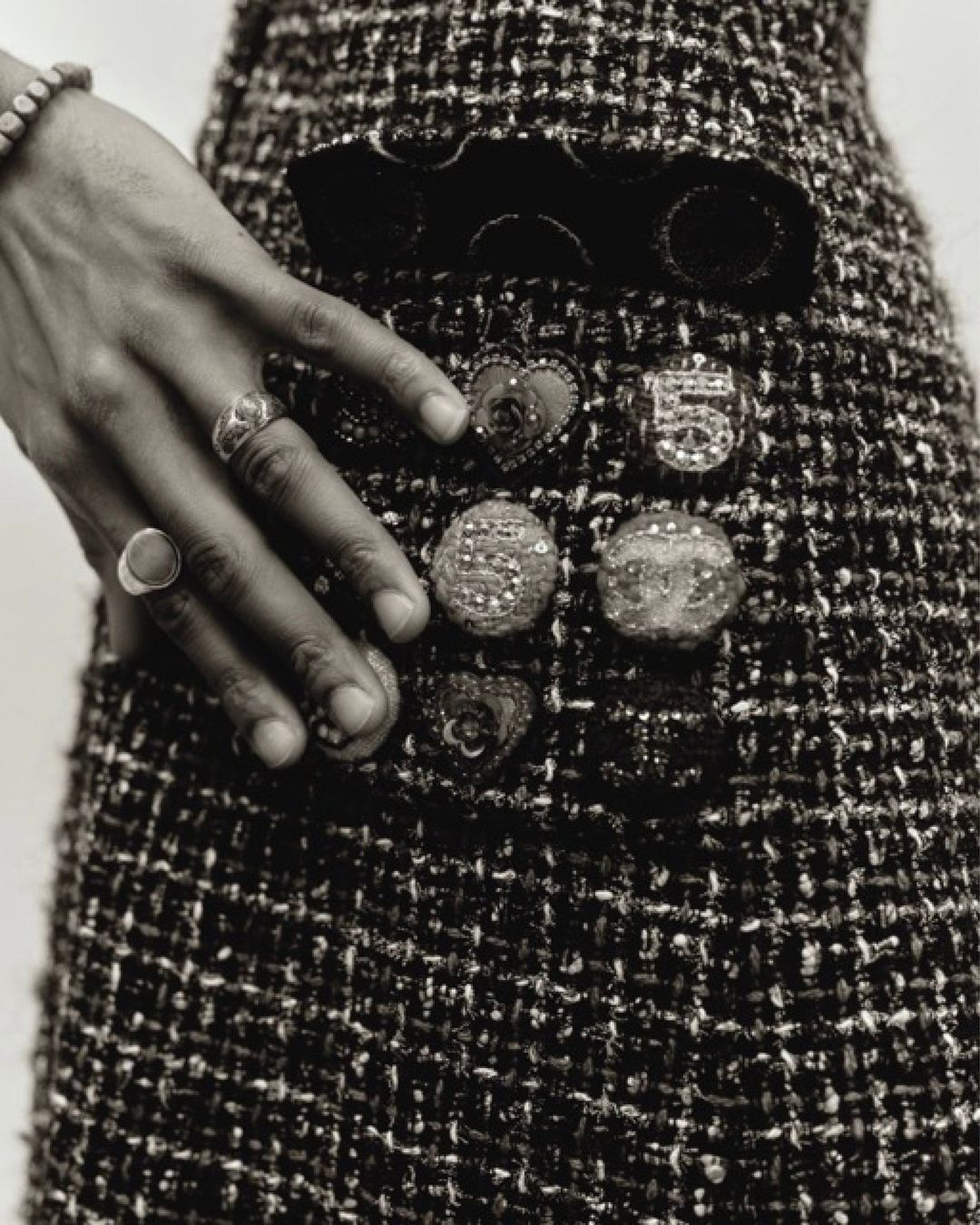 Close-up of tweed skirt with decorative buttons and a hand adorned with rings resting on it, black and white. Fashion.