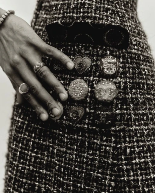 Close-up of tweed skirt with decorative buttons and a hand adorned with rings resting on it, black and white. Fashion.
