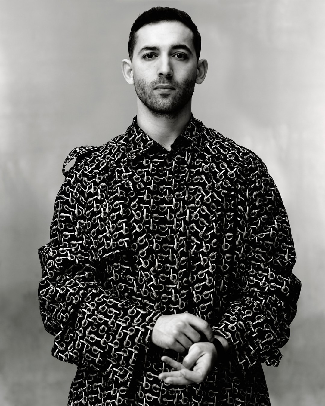 Monochrome portrait of adult male wearing patterned overcoat in a medium studio shot against a neutral background with soft lighting.