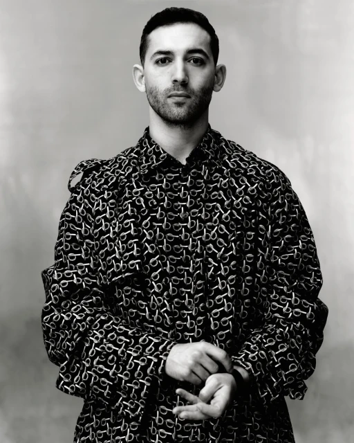 Monochrome portrait of adult male wearing patterned overcoat in a medium studio shot against a neutral background with soft lighting.