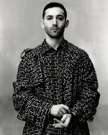 Monochrome portrait of adult male wearing patterned overcoat in a medium studio shot against a neutral background with soft lighting.