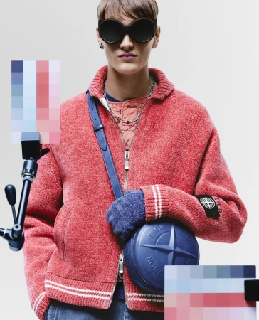 Fashionable individual with sunglasses poses indoors, wearing a red jacket, carrying a blue round purse, and standing against a neutral backdrop.
