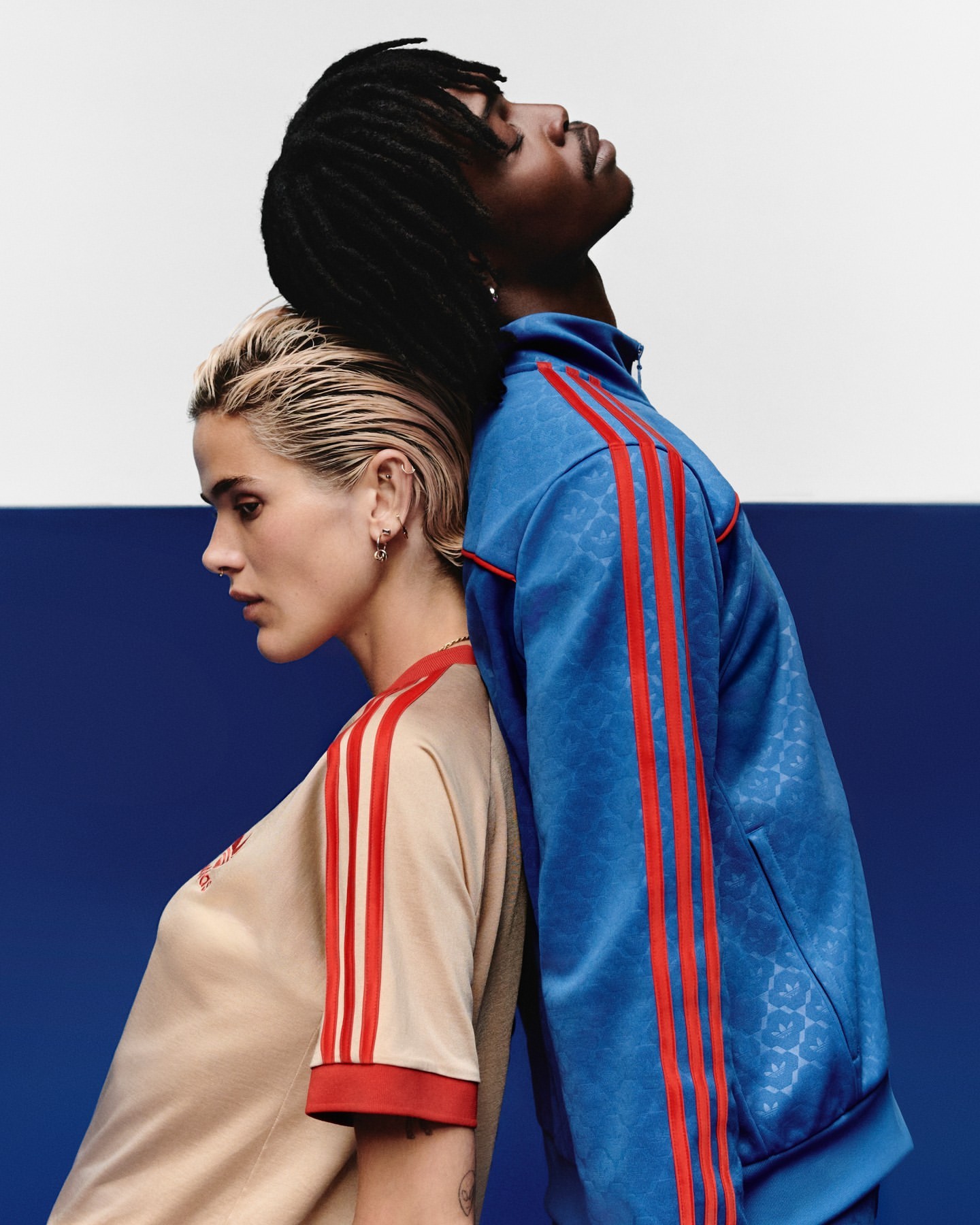 Portrait of a young adult couple in sportswear leaning back-to-back against a backdrop of white and blue. Fashion and sport concept.
