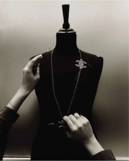 Black and white studio shot of a mannequin being prepared for a fashion shoot with hands pinning a Chanel brooch.