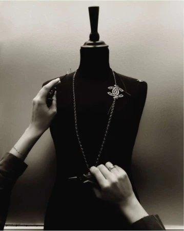 Black and white studio shot of a mannequin being prepared for a fashion shoot with hands pinning a Chanel brooch.