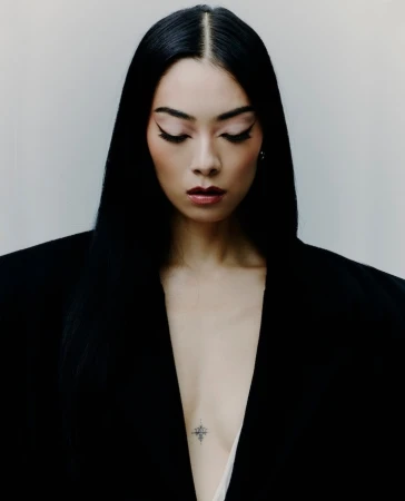 Portrait of a woman with long black hair wearing a structured black blazer against a plain white background by Ethan Hart
