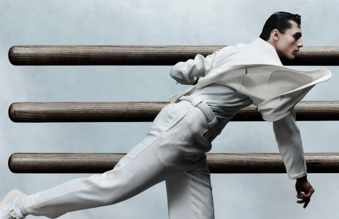 Man wearing white apparel in motion against horizontal wooden bars in London by Ethan Hart
