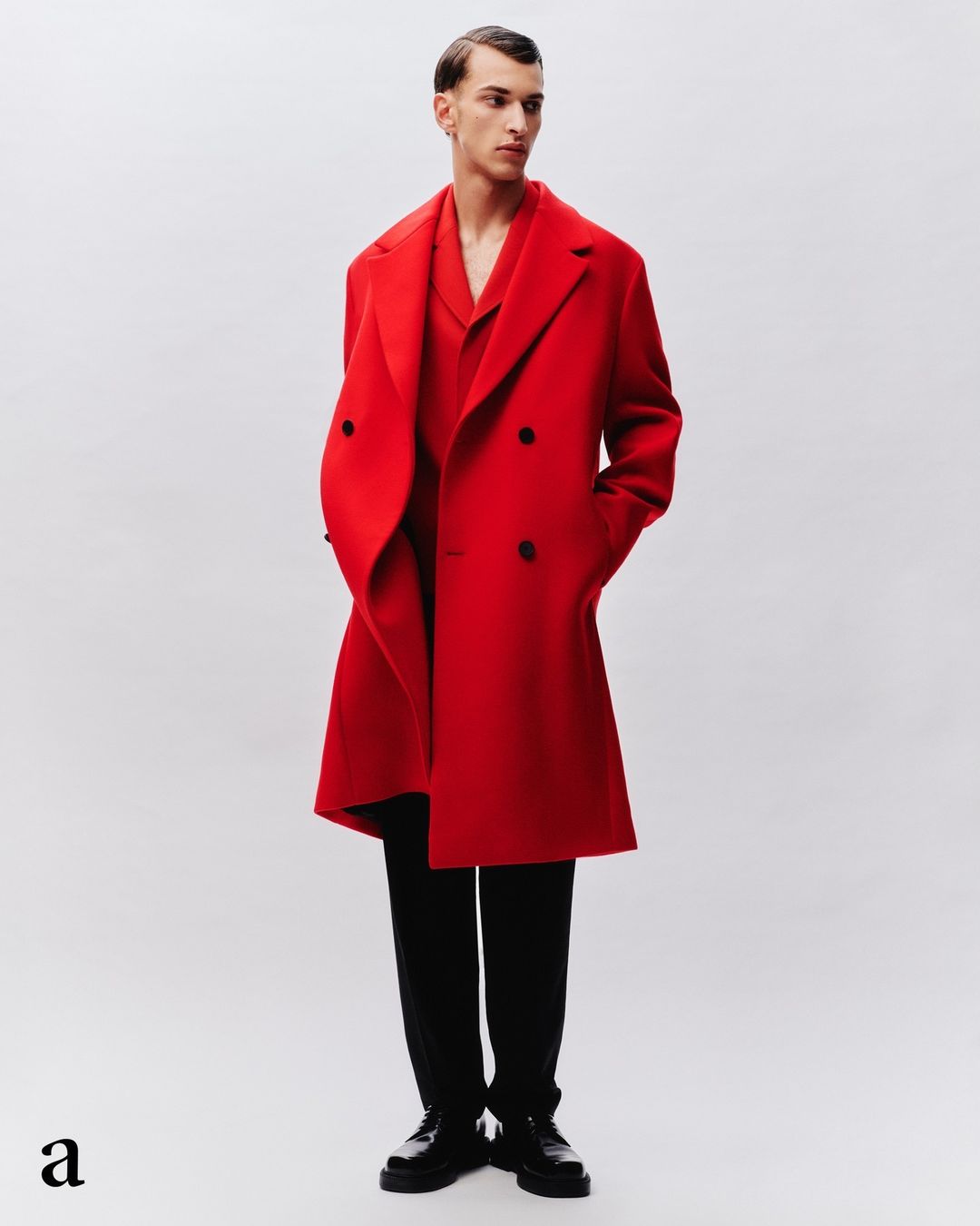 Man in a vibrant red double-breasted overcoat, matching shirt, black pants, and dress shoes, posing in a clean photo studio setting.
