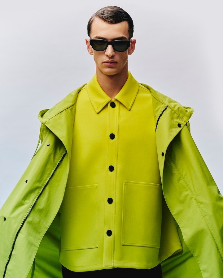 Man wearing black sunglasses and a bright lime green buttoned jacket against a pale grey seamless background.