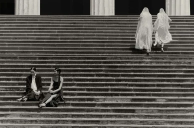 Four women on large stone steps, two seated on the lower left and two walking up the stairs in light draped garments