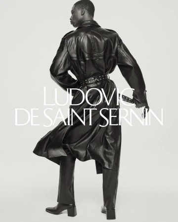 Editorial fashion shot of a Black male model in a black leather coat and pants. He has his back to the viewer in a studio environment.