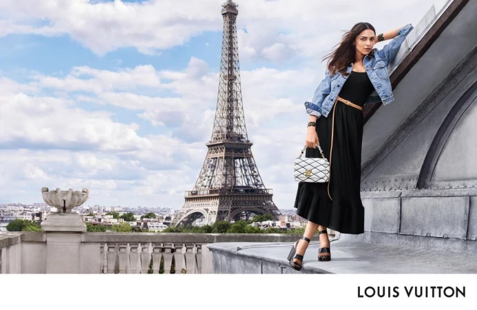 Woman in black dress and denim jacket leaning on a rooftop ledge with the Eiffel Tower in the background