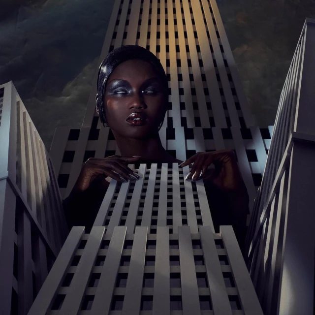 Stunning portrait of a Black woman with glitter eyeshadow, shiny lip gloss, and long nails, posed with geometric architectural shapes.