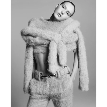 Black and white portrait of a model wearing a furry knit sweater and pants, posing with her head tilted and hands on hips.