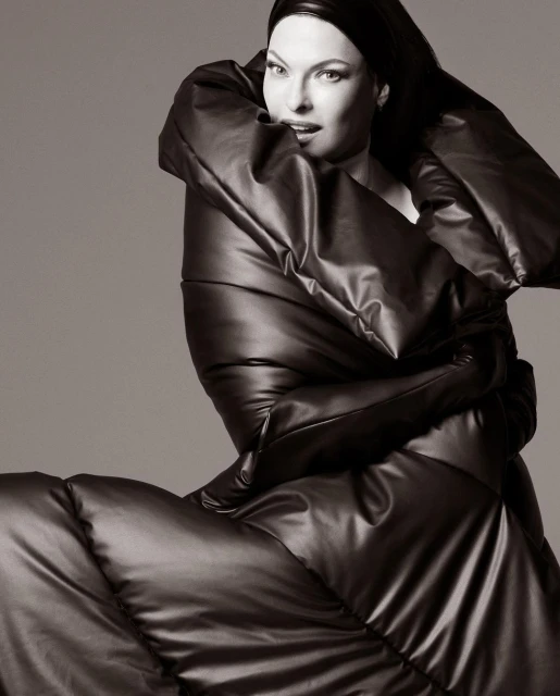 Fashionable woman in oversized puffer coat and head covering poses against a neutral backdrop. Black and white, studio lighting.