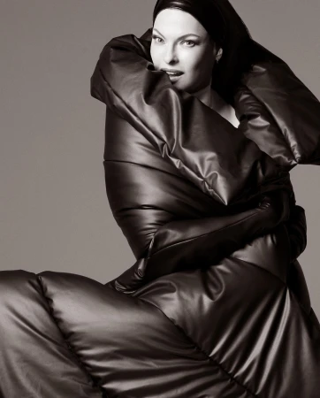 Fashionable woman in oversized puffer coat and head covering poses against a neutral backdrop. Black and white, studio lighting.