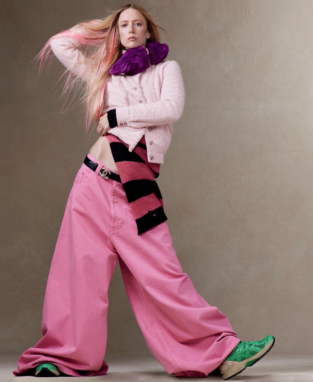 Fashion portrait of a stylish adult woman with pink-streaked hair, wearing an outfit featuring a pink sweater and wide-leg jeans.