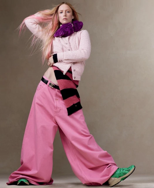Fashion portrait of a stylish adult woman with pink-streaked hair, wearing an outfit featuring a pink sweater and wide-leg jeans.