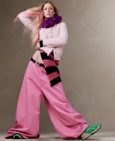 Fashion portrait of a stylish adult woman with pink-streaked hair, wearing an outfit featuring a pink sweater and wide-leg jeans.