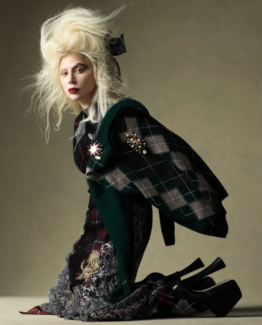 A fair-skinned woman with blonde hair, red lips, and a tartan outfit poses kneeling with stacked platform heels in a studio shot.