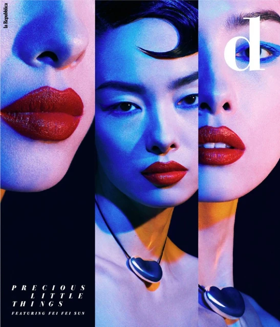 Close-up studio shot of a stylish Asian woman with red lipstick and blue eyeliner, wearing a heart-shaped necklace against a dark background.
