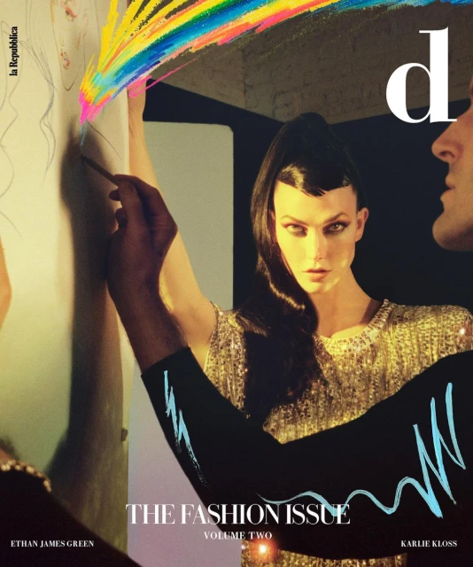 Fashion magazine cover featuring a model with dark hair and a shimmering gold dress, drawing colorful lines on a wall, with a man's face visible.