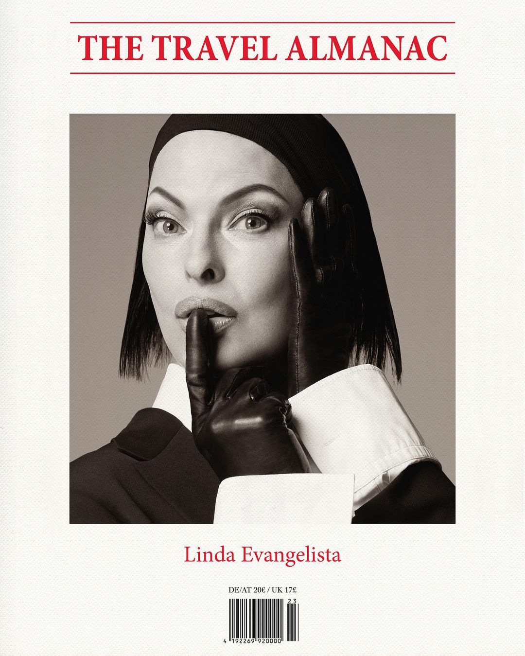 Black and white portrait of Linda Evangelista on the cover of The Travel Almanac, wearing black gloves and a dark suit, holding finger to lips.