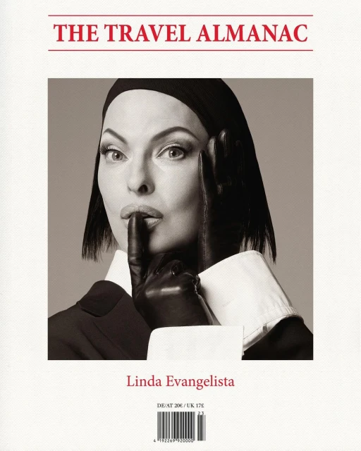 Black and white portrait of Linda Evangelista on the cover of The Travel Almanac, wearing black gloves and a dark suit, holding finger to lips.