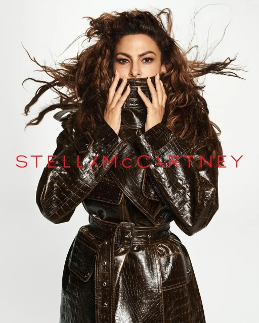 Brunette woman in an eye-catching brown leather trench coat. Her hair is windblown, and the backdrop is a clean white in a fashion shoot.