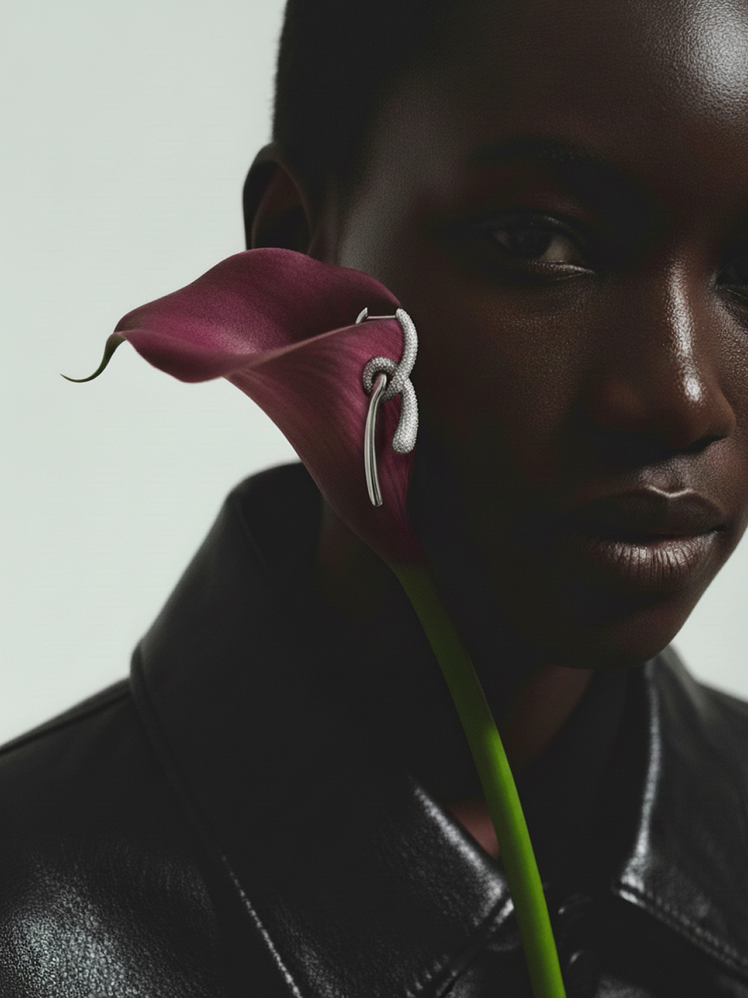 Close-up fashion shot of an African-descent woman wearing an ear ring, posing with a calla lily against a bright white background.