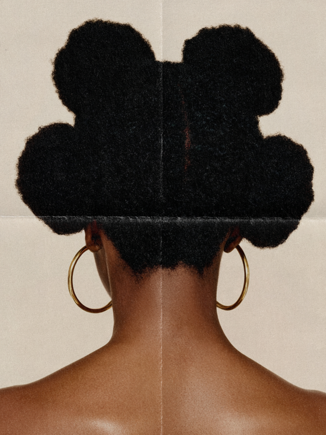 Back view of a black woman with natural afro hair styled in buns, wearing large gold hoop earrings against a folded light beige background.