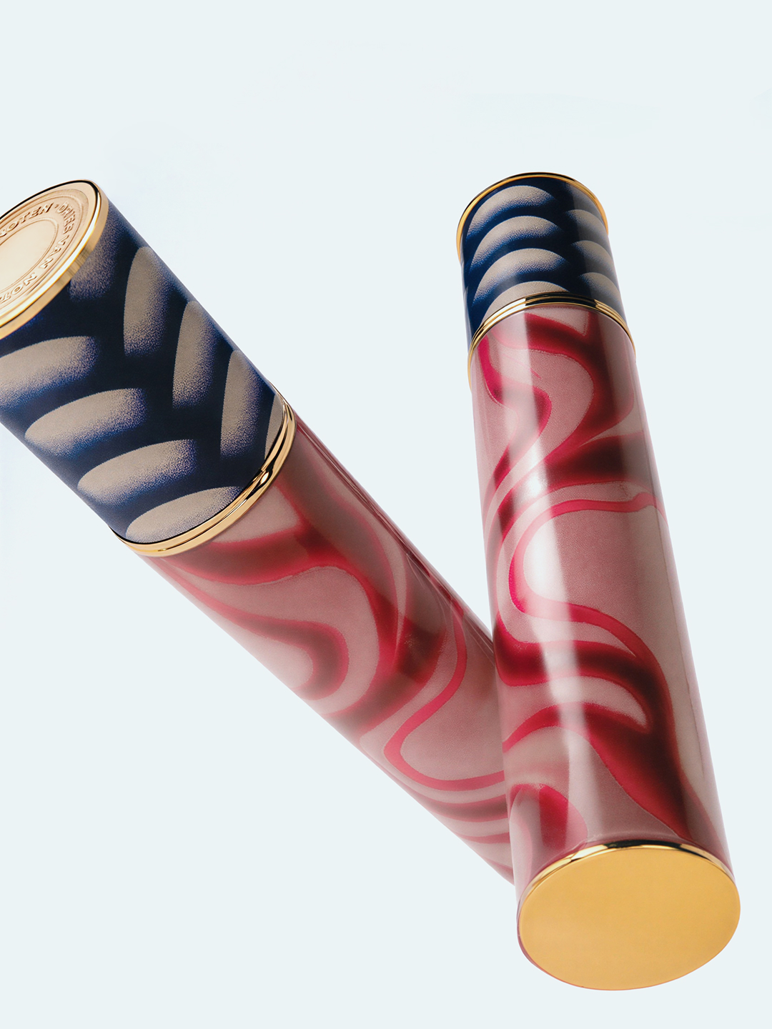 Two cylindrical cosmetic containers in pink and blue with gold lids and bases on a white backdrop, photographed at a low angle.
