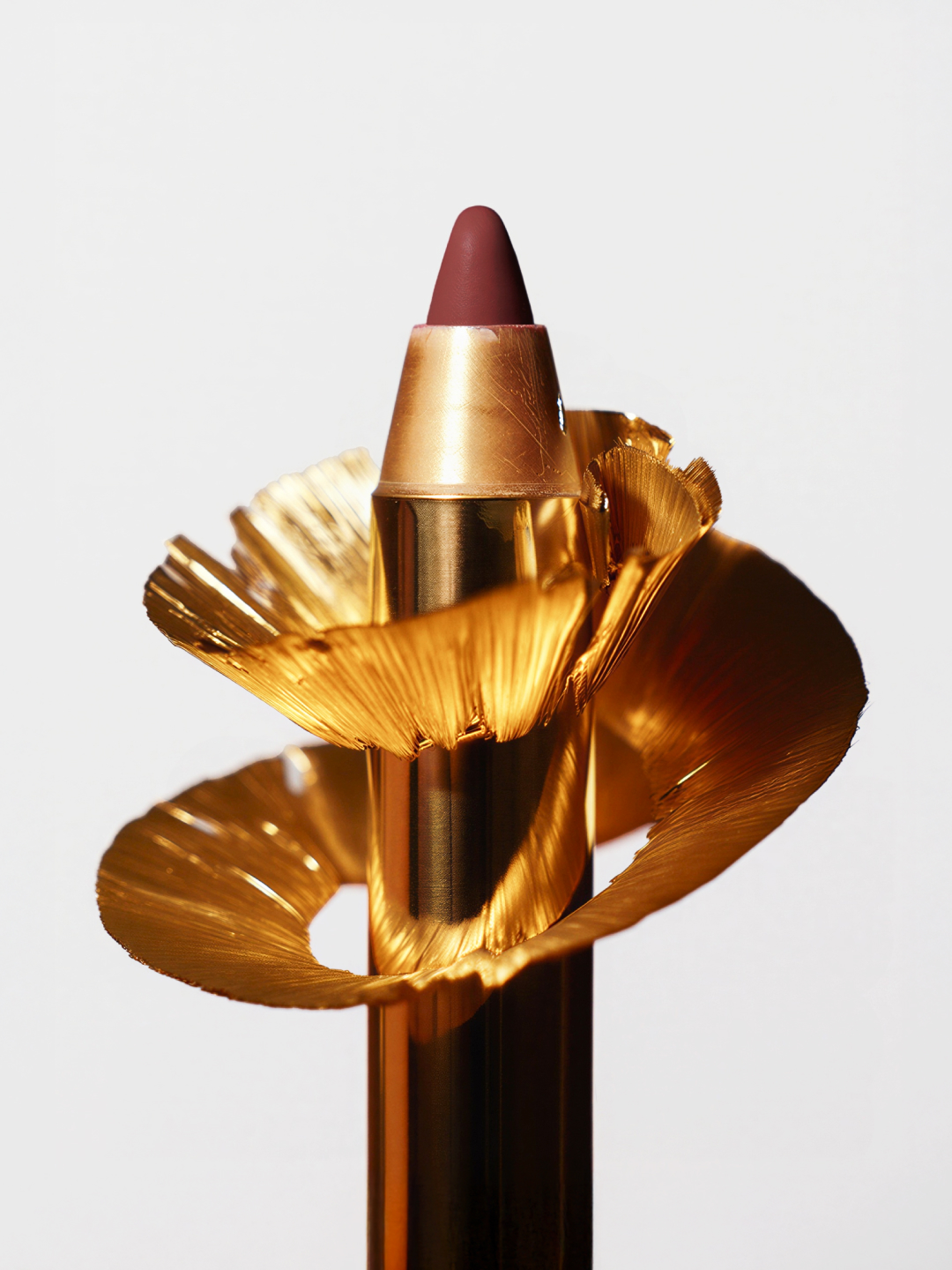Elegant still life featuring a makeup crayon with gold metallic shavings on a white background, highlighting beauty and cosmetic artistry.