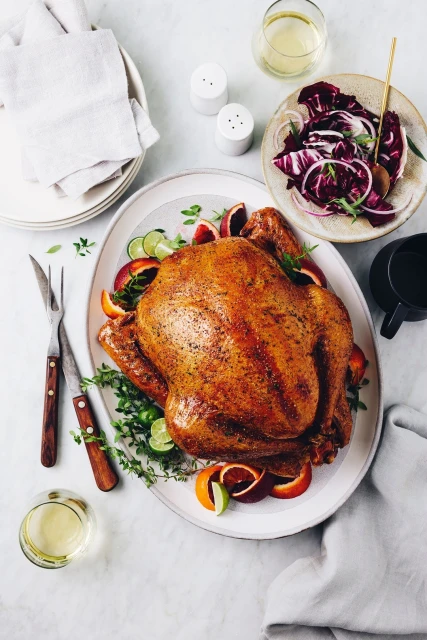Overhead shot of a roasted turkey garnished with citrus slices and thyme on an oval platter, accompanied by salad, salt shakers, and drinks.