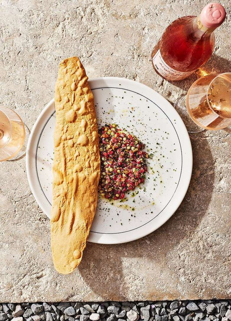 Overhead shot of a plate featuring artisanal bread, a salad, rose wine bottle, and glasses on a stone surface, food photography.