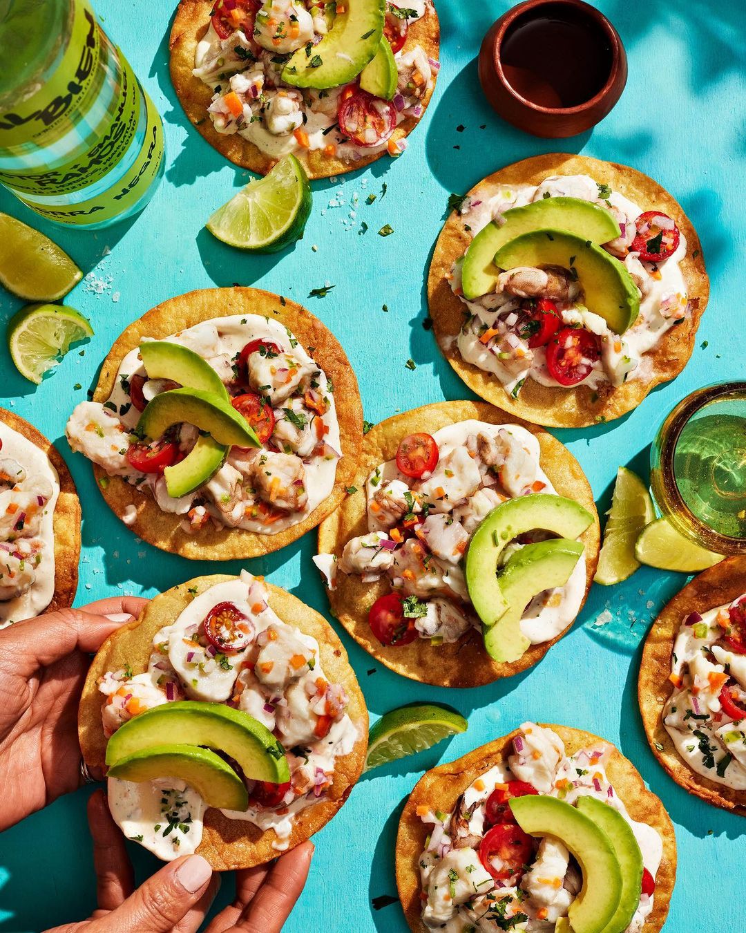 Overhead shot of tostadas topped with shrimp ceviche, avocado, and lime arranged on a bright blue surface, highlighting fresh ingredients.
