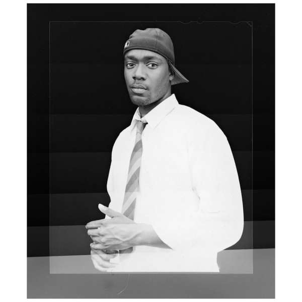 Black-and-white portrait of a man wearing a baseball cap and collared shirt with a tie, shot by Evan Klanfer.
